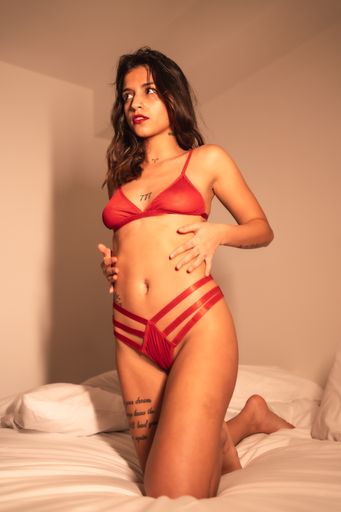 An attractive brunette Spanish woman with tattoos in underwear in a sensual pose on the bed