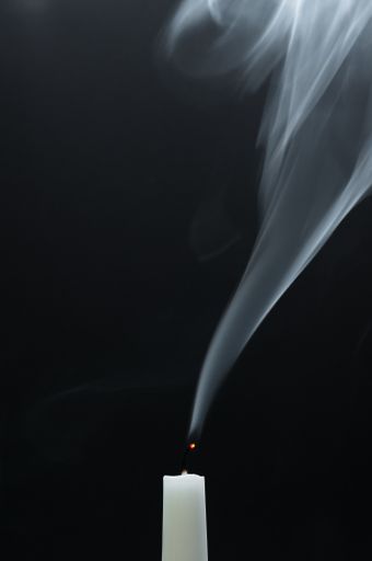 A vertical shot of a smoking white candle on a black background