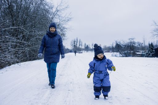 A young happy mommy with her little son walking with a wooden sled on snow at a park on a cold winter day