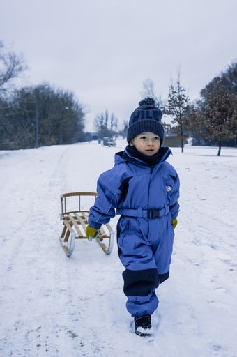A cute adorable little boy in winterwear pulling a wooden sled at a park on a cold winter day