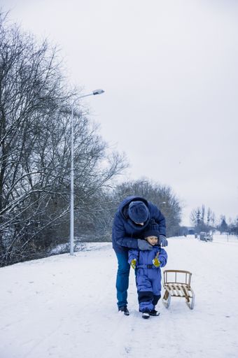 A vertical shot of a young mother adjusting the winter overall of her little cute son at a park