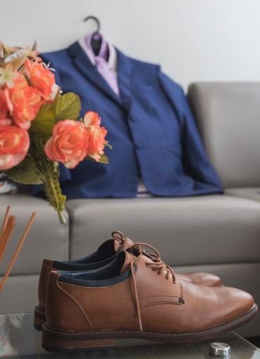 A vertical shot of a pair of brown derby shoes on the table with a suit in the background