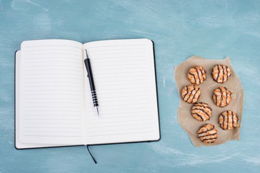 Coconut macaroons on a textured blue background, empty booklet with a pen, christmas time
