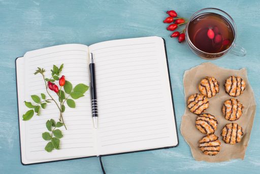 Coconut macaroons on a textured blue background, empty booklet with a pen, cup of tea