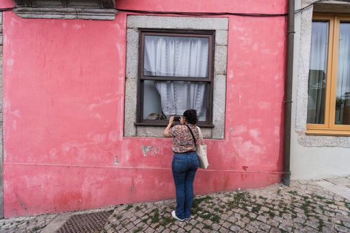 A closeup shot of a woman taking a photo of a cat sitting near the window of a red house