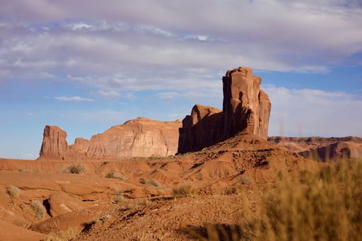 Scenic view of Monument Valley's iconic red sandstone buttes under a partly cloudy sky, showcasing the stunning desert landscape.