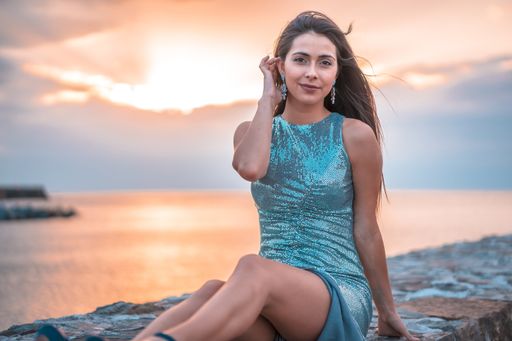 An attractive young brunette woman wearing sequin dress sitting near the sea during the sunrise in San Sebastian, Spain