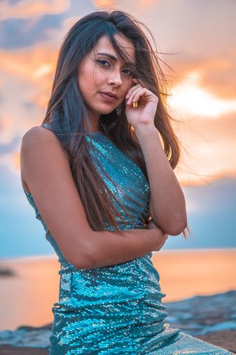 An attractive young brunette woman wearing sequin dress sitting near the sea during the sunrise in San Sebastian, Spain