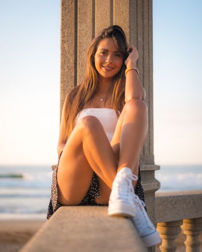 A vertical shot of a smiling brunette woman sitting on a concrete surface in Zarautz, Spain
