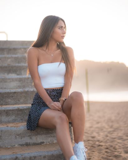 A vertical shot of an attractive brunette sitting on concrete stairs at the beach in Zarautz, Spain