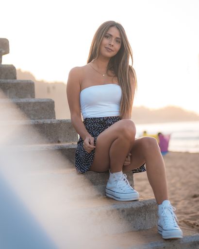 A vertical shot of a smiling brunette woman sitting on concrete stairs at the beach in Zarautz, Spain