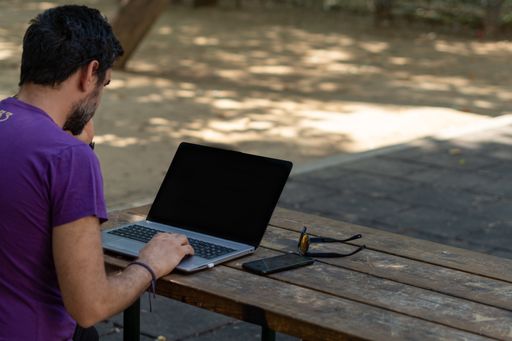 young man working at his computer on a wooden table in the park on a sunny day