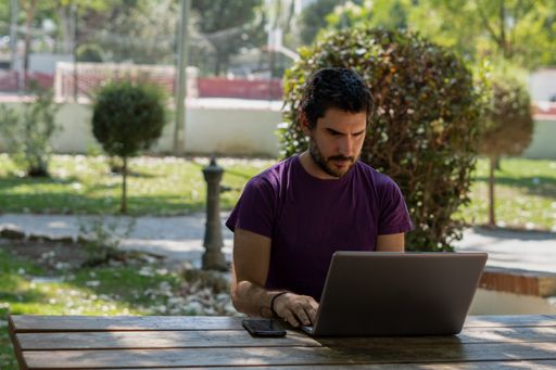 young man working at his computer on a wooden table in the park on a sunny day