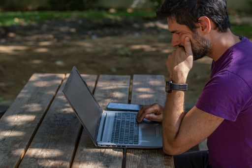 young man working at his computer on a wooden table in the park on a sunny day