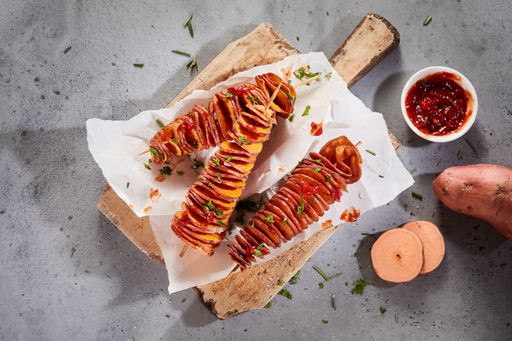The deep-fried spiral sweet potatoes served with tomato sauce and fresh green herbs on a wooden board