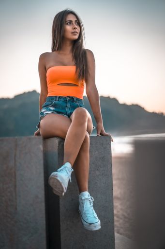 A vertical shot of an attractive brunette sitting on a concrete surface at the beach in Zarautz, Spain