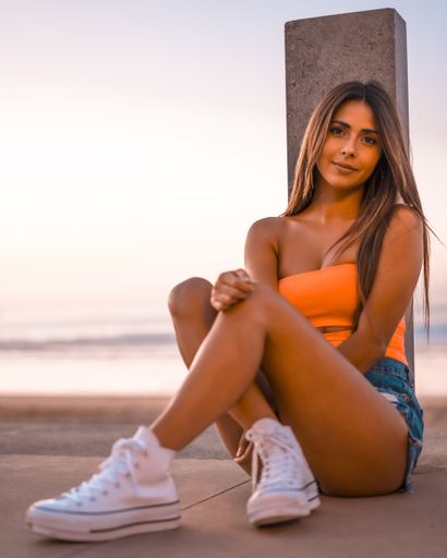 A vertical shot of an attractive brunette sitting on a concrete surface at the beach in Zarautz, Spain