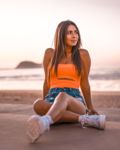 A vertical shot of an attractive brunette sitting on a concrete surface at the beach in Zarautz, Spain