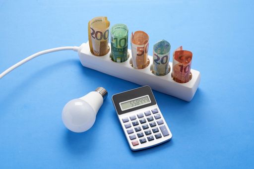 An electric plug strip with euro banknotes, light bulb and a calculator isolated on a blue background