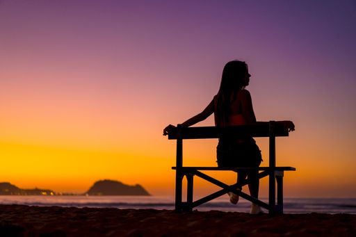 A silhouette of a woman sitting on a bench in Zarautz, Spain with a beautiful sunset in the background