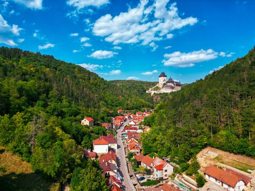 Aerial view of Karlstejn Castle, surrounded by lush greenery and village houses under a vibrant blue sky.