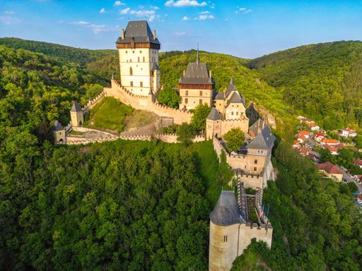 Aerial view of Karlstejn Castle with lush green forests and clear blue sky in Czech Republic.