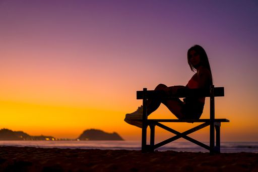 A young brunette woman's silhouette sitting on a bench near the sea during the sunset