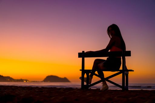 A young brunette woman's silhouette sitting on a bench near the sea during the sunset