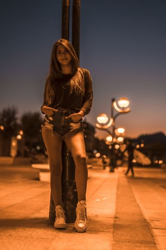 A vertical shot of a beautiful female standing by a street lamp captured at night in Zarautz, Spain