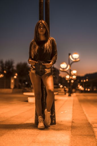 A vertical shot of an attractive brunette leaning against the lamppost in Zarautz, Spain