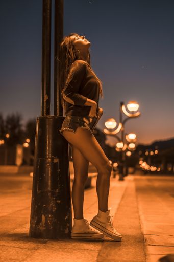 A vertical shot a young elegant female standing in front of a column and looking at the night sky