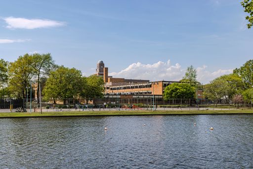 A scenic view of Central High School with a clock tower by the pond in Hendrickson Park, surrounded by lush greenery under blue skies.