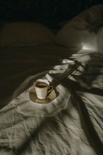 A cup of tea on a white rumpled bed in an aesthetic environment