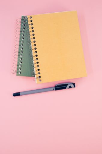 A vertical shot of closed notebook on a pink background with copy space