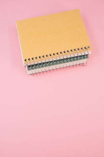 A vertical shot of closed notebook on a pink background with copy space