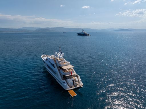 Luxury yachts anchored in clear blue waters under a sunny sky with distant hills visible on the horizon.