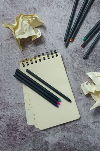 Notebook with pens and crumpled paper on a textured surface