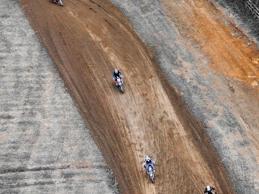 Aerial view of motocross riders racing on a dirt track, showcasing speed and skill on a rugged terrain.