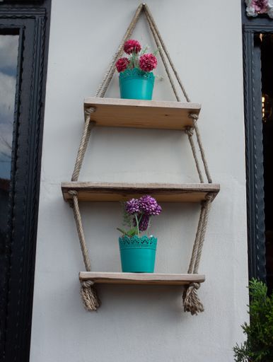A vertical shot of hanging wooden shelves on ropes with potted plants on it