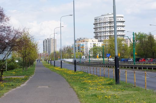 A narrow empty asphalt footpath by a road and apartment blocks under a blue cloudy sky in Poznan