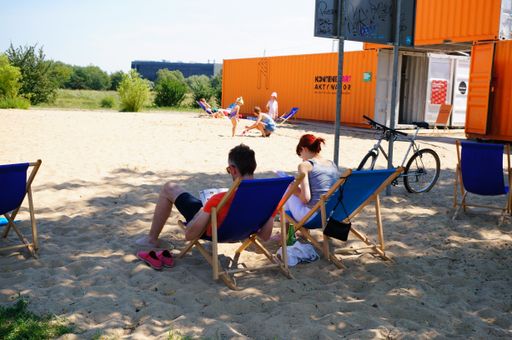A back view of people sitting on beach loungers on a sunny day at a sandy beach