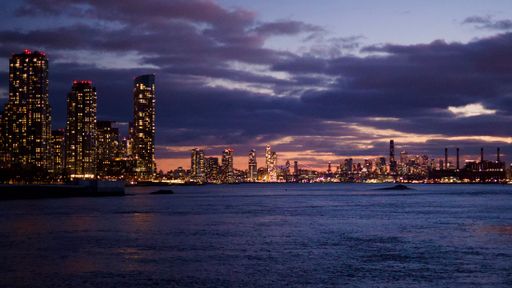 A stunning view of New York City's skyline at dusk with illuminated skyscrapers and a serene river in the foreground.
