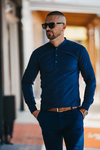 A cool handsome Caucasian man wearing an elegant blue shirt and sunglasses posing outdoor