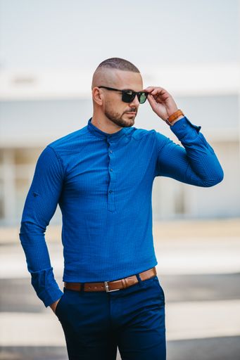 A cool handsome Caucasian man wearing an elegant blue shirt and sunglasses posing outdoor