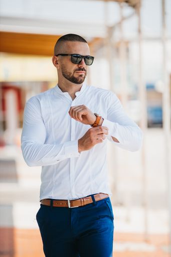 A cool handsome Caucasian man wearing an elegant white shirt and sunglasses posing outdoor