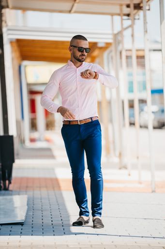 A cool handsome Caucasian man wearing an elegant light pink shirt and sunglasses posing outdoor