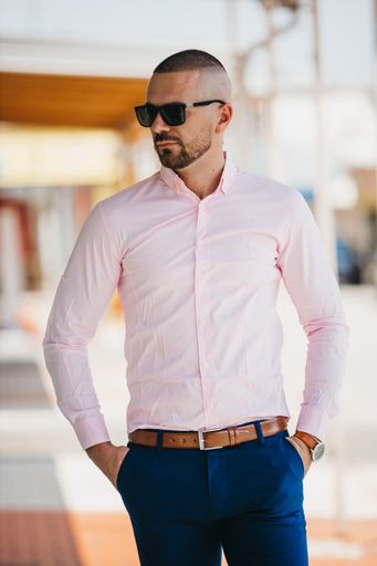 A cool handsome Caucasian man wearing an elegant light pink shirt and sunglasses posing outdoor