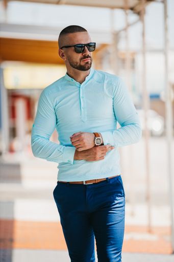 A cool handsome Caucasian man wearing an elegant light blue shirt and sunglasses posing outdoor