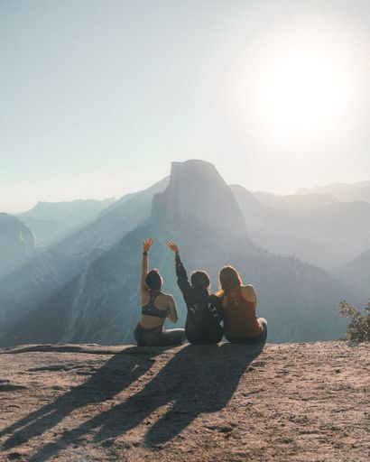 A vertical shot of friends sitting on a rocky hill on a sunny day