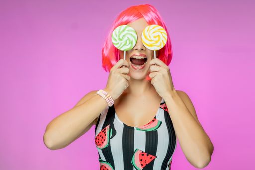 A white woman holding lollipops in front of her eyes on a pink background